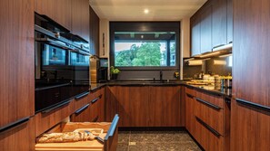A modern kitchen with wooden cabinets, a built-in oven, and a window overlooking greenery. - Villa Tauris - Lake Lucerne - Private Spa & Natural Pool (Emmetten)