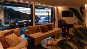 Un salon moderne avec un canapé, une table d’échecs et une vue sur un plan d’eau et des montagnes.