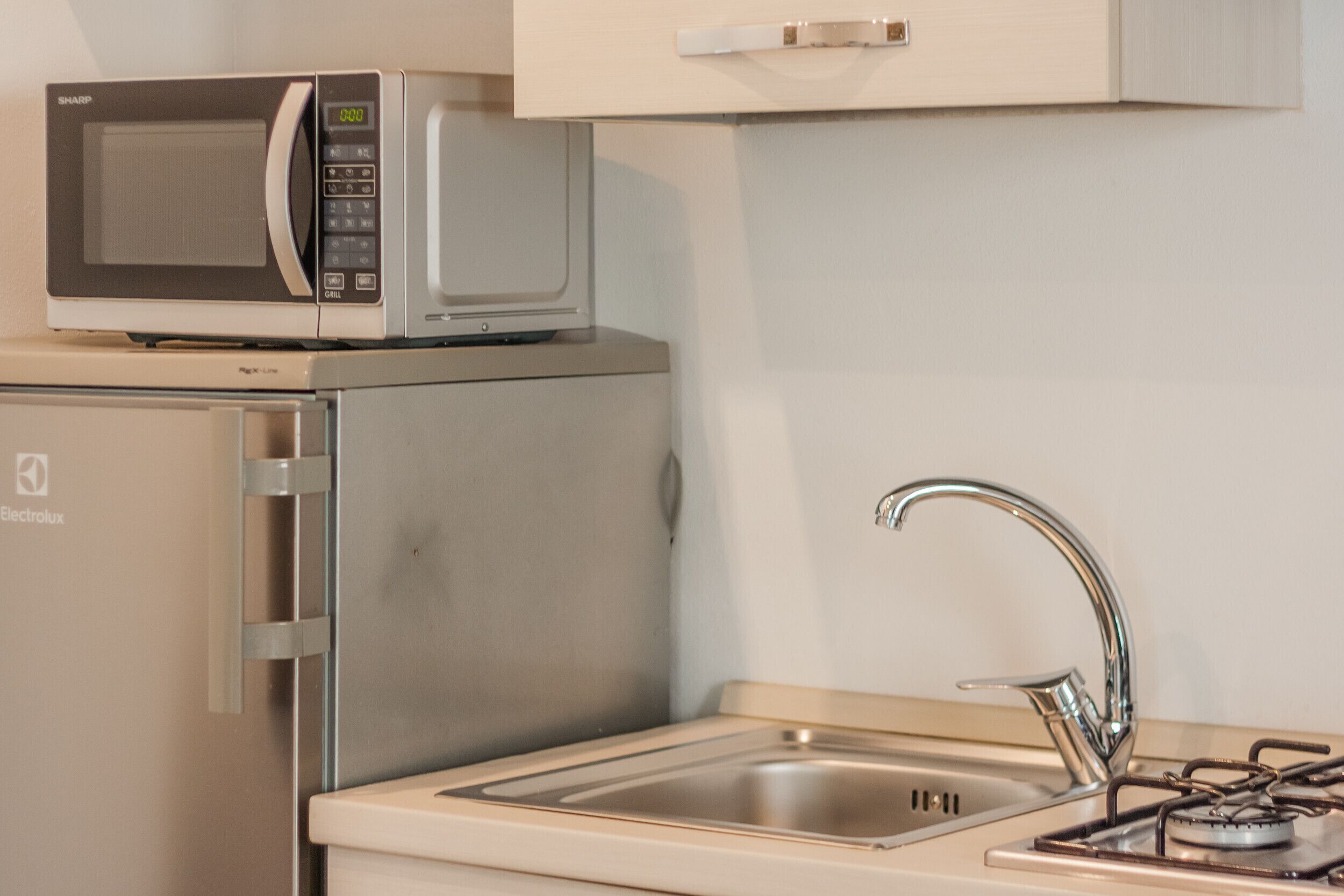 A compact kitchen with a microwave, a refrigerator, a sink, and a gas stove.