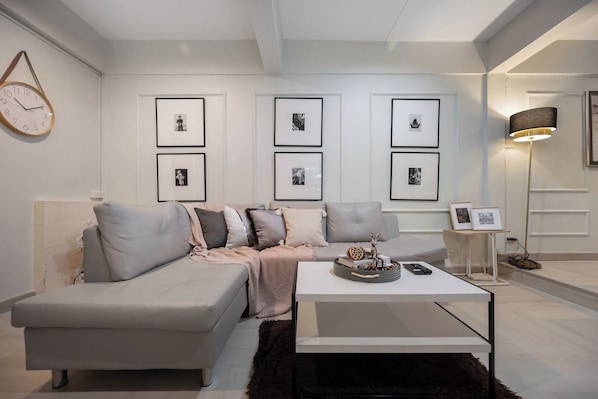 Un salon moderne avec un canapé gris, une table basse blanche et des tableaux encadrés accrochés au mur.