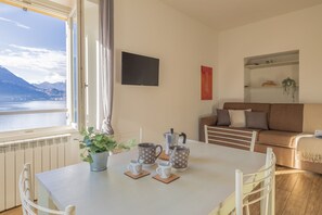 Ein Essbereich mit Tisch für zwei Personen, einem Blumentopf und Blick auf einen See mit Bergen im Hintergrund.