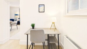 A modern dining area with a wooden table, a grey chair, a small potted plant, and a floor lamp. - *NEW* Artisan Court | Central | Modern | Parking (Gloucestershire)