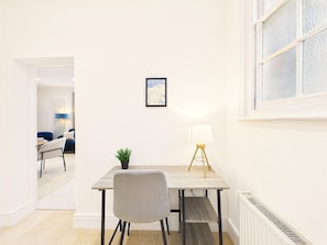 Et moderne spiseområde med et træbord, en grå stol, en lille potteplante og en gulvlampe.