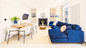 A modern living room with a blue sofa, a dining table with chairs, and a fireplace. - *NEW* Artisan Court | Central | Modern | Parking (Gloucestershire)