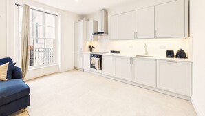 A modern kitchen with white cabinets, a built-in oven, and a window with curtains. - *NEW* Artisan Court | Central | Modern | Parking (Gloucestershire)