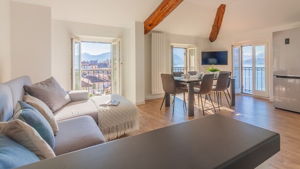 A modern apartment with a dining area, kitchen, and a large window offering a view of the mountains. - Above the Lake by Varenna Holidays (Varenna)