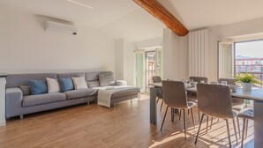A modern living room with a grey sofa, wooden flooring, and a dining area with chairs and a table. - Above the Lake by Varenna Holidays (Varenna)