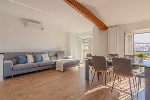 Ein modernes Wohnzimmer mit grauem Sofa, Holzboden und einem Essbereich mit Stühlen und Tisch.