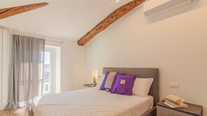 A bedroom with a bed, a nightstand, a window with curtains, and a wooden ceiling beam. - Above the Lake by Varenna Holidays (Varenna)