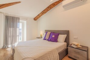 Ein Schlafzimmer mit einem Bett, einem Nachttisch, einem Fenster mit Vorhängen und einem Holzbalken an der Decke.