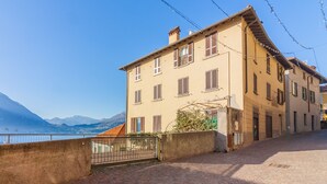 A two-story building with a brick facade, a metal gate, and a view of a body of water and mountains in the background. - Above the Lake by Varenna Holidays (Varenna)