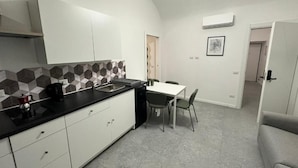 Cocina compacta con armarios blancos, encimera negra y salpicadero de azulejos hexagonales.