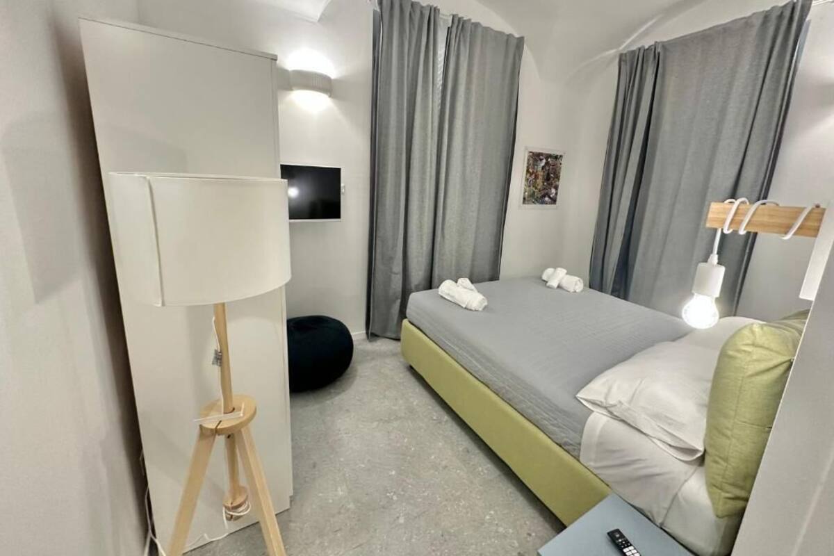 A modern hotel room with a bed, a bedside lamp, a flat-screen TV, and a small table.