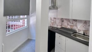 Una cocina compacta con armarios blancos, una encimera negra y una ventana con celosía metálica.