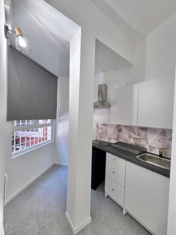 A compact kitchen with white cabinets, a black countertop, and a window with a metal grid.