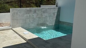 Une piscine extérieure moderne, avec un mur en pierre et un petit marchepied menant à l’eau.