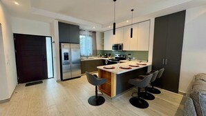 Une cuisine moderne dotée d’un îlot central, d’appareils électroménagers en acier inoxydable et de tabourets de bar.