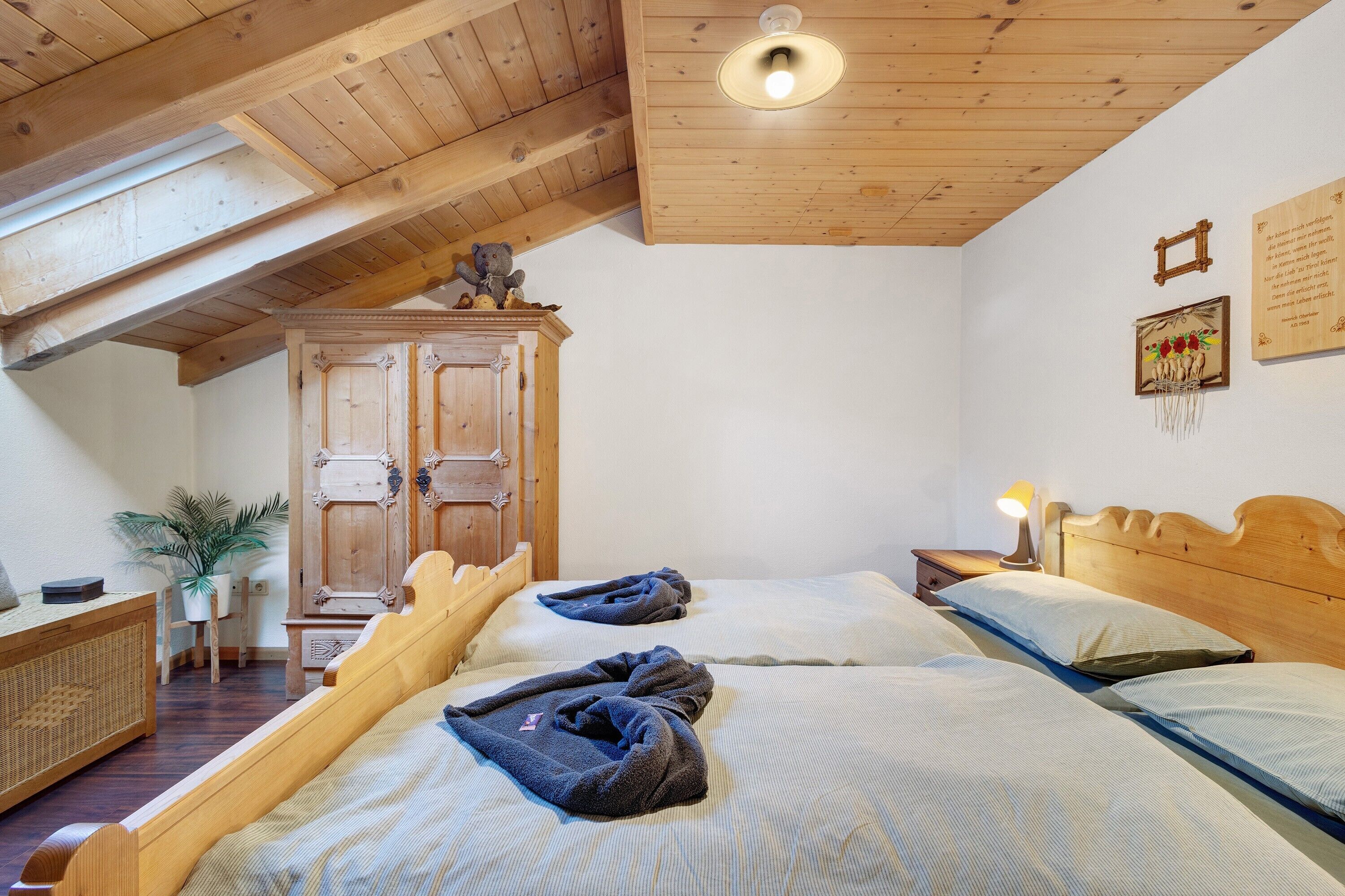 Una stanza con due letti, travi a vista in legno, un armadio in legno, un comodino con una lampada e una parete con quadri.