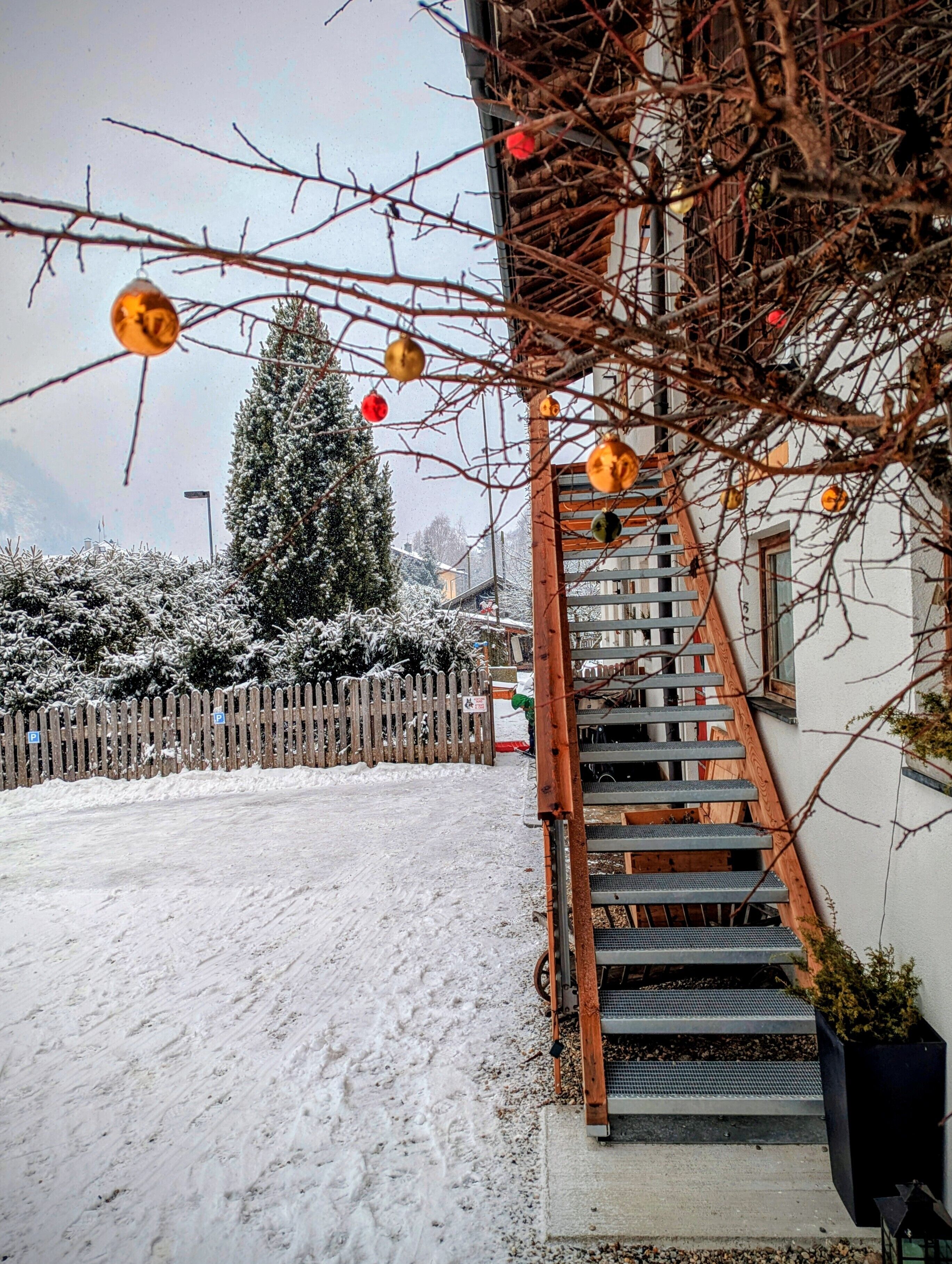 Un espace extérieur enneigé, agrémenté d’une clôture en bois, d’un escalier et d’un sapin de Noël.