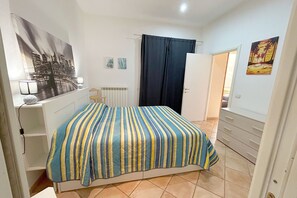A bedroom with a bed, a radiator, a window with a view of the city, and a door leading to another room. - La Casa di Marco near the sea (Marina di Grosseto)