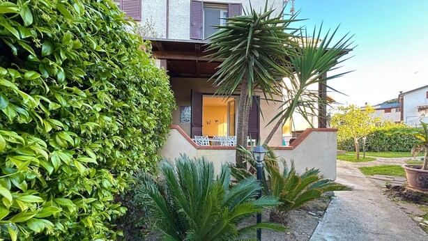 Un edificio residencial con un porche cubierto, una palmera y un jardín bien cuidado.