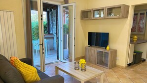 Una sala de estar con sofá, una mesa de centro, un televisor sobre un mueble de madera y una puerta corrediza de vidrio que da a un área exterior.