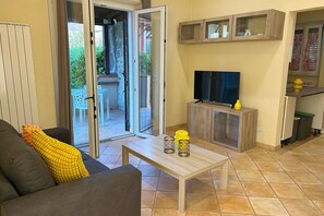 A living room with a sofa, a coffee table, a TV on a wooden cabinet, and a sliding glass door leading to an outdoor area. - La Casa di Marco near the sea (Marina di Grosseto)
