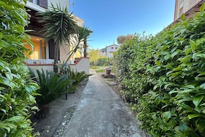 A narrow pathway flanked by lush greenery and buildings with balconies. - La Casa di Marco near the sea (Marina di Grosseto)