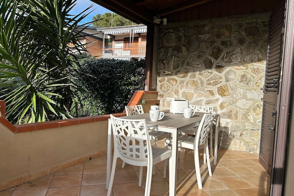 A patio with a stone wall, white outdoor furniture, and a view of a building in the background. - La Casa di Marco near the sea (Marina di Grosseto)