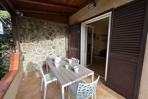 A patio with a stone wall, a wooden table, and white chairs. - La Casa di Marco near the sea (Marina di Grosseto)