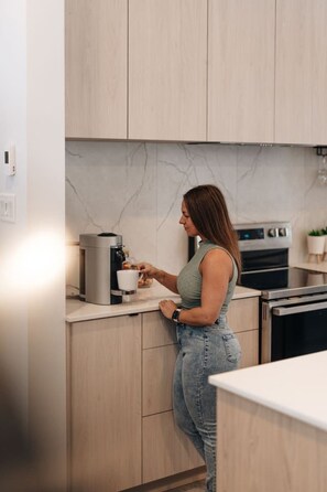 Una persona en una cocina moderna con armarios de madera, un protector contra salpicaduras de mármol y una máquina de café.
