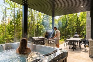 Ein Außenbereich mit Whirlpool, Grill und Essbereich, umgeben von Bäumen.