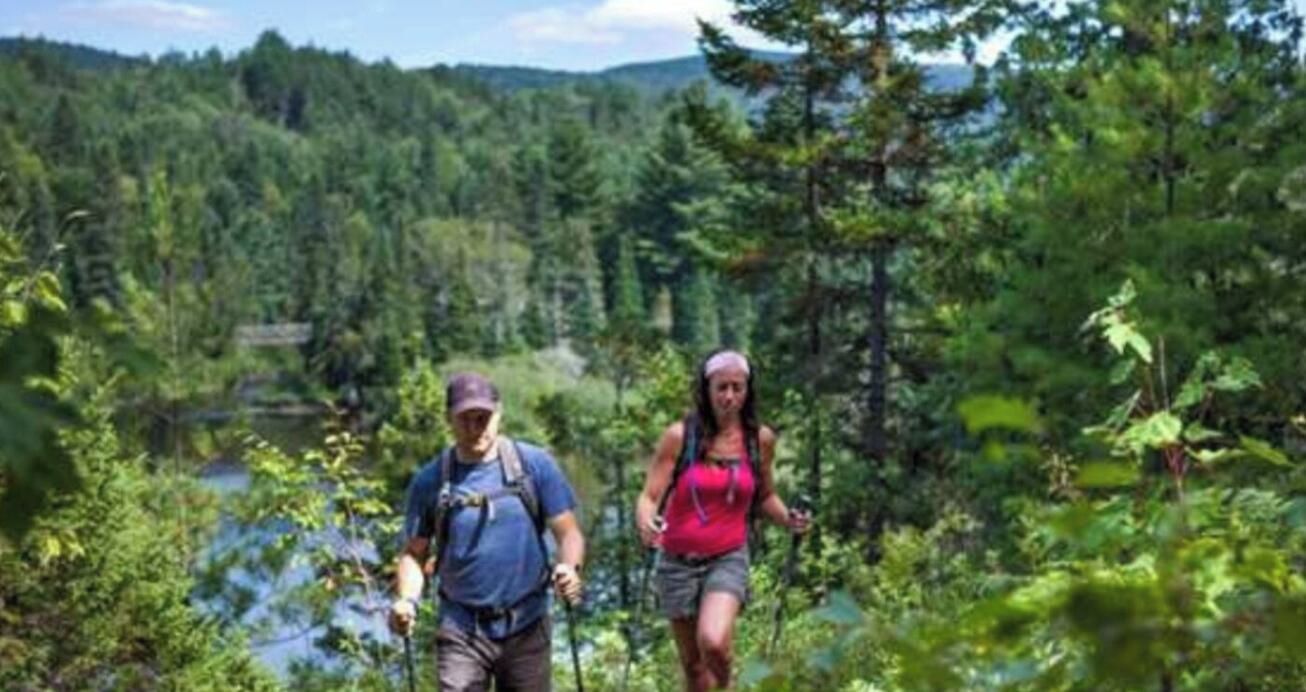 Two people hiking in a forested area with a lake in the background.
