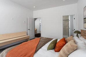 Un dormitorio con cama, un banco y una puerta que da a otra habitación.
