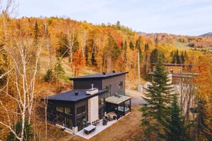 Ein modernes, zweistöckiges Haus mit Terrasse, umgeben von einer bewaldeten Landschaft.