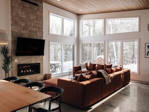 Una sala moderna con chimenea de piedra, un sofá grande y un comedor con sillas.