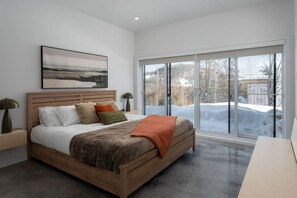 Ein Schlafzimmer mit einem großen Bett, einem Holzkopfteil, einem Bild an der Wand und Blick auf eine verschneite Landschaft durch eine Glastür.