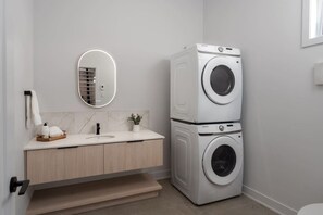 A modern bathroom with a built-in washer and dryer, a marble-tiled vanity, a mirror, and a small potted plant. - Vitalité | Private Spa, Sauna & Pool table (Saint-Côme)