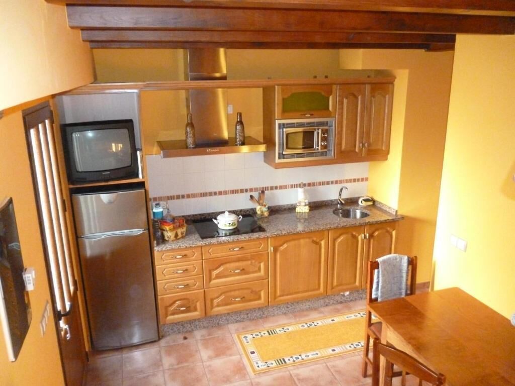 Cocina compacta con refrigerador, microondas y estufa. Cuenta con gabinetes de madera y salpicadero de azulejos.