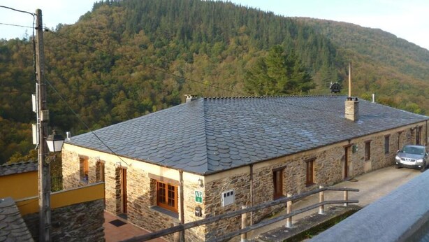 A stone building with a tiled roof, a car parked in front, and a forested hill in the background. - Apartamentos Rurales Veredas (Santa Eulalia de Oscos)