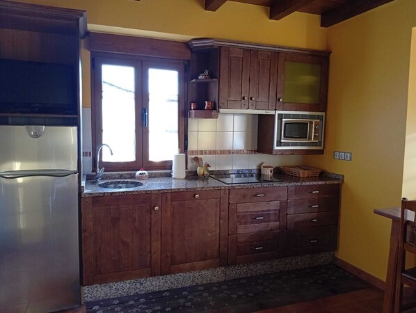Una cucina con mobili in legno, un frigorifero in acciaio inossidabile, un forno a microonde e una finestra con persiane.