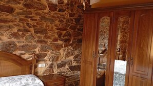 A bedroom with a stone wall, wooden wardrobe, and a bed with a floral bedspread. - Apartamentos Rurales Veredas (Santa Eulalia de Oscos)