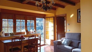 A dining area with a wooden table and chairs, a chandelier, and a sofa. - Apartamentos Rurales Veredas (Santa Eulalia de Oscos)