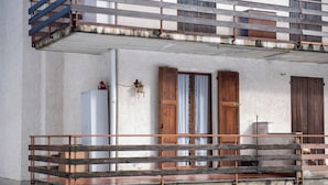 A balcony with a wooden railing, a white wall, and a window with a curtain. - Casa Eleonora (Zogno)