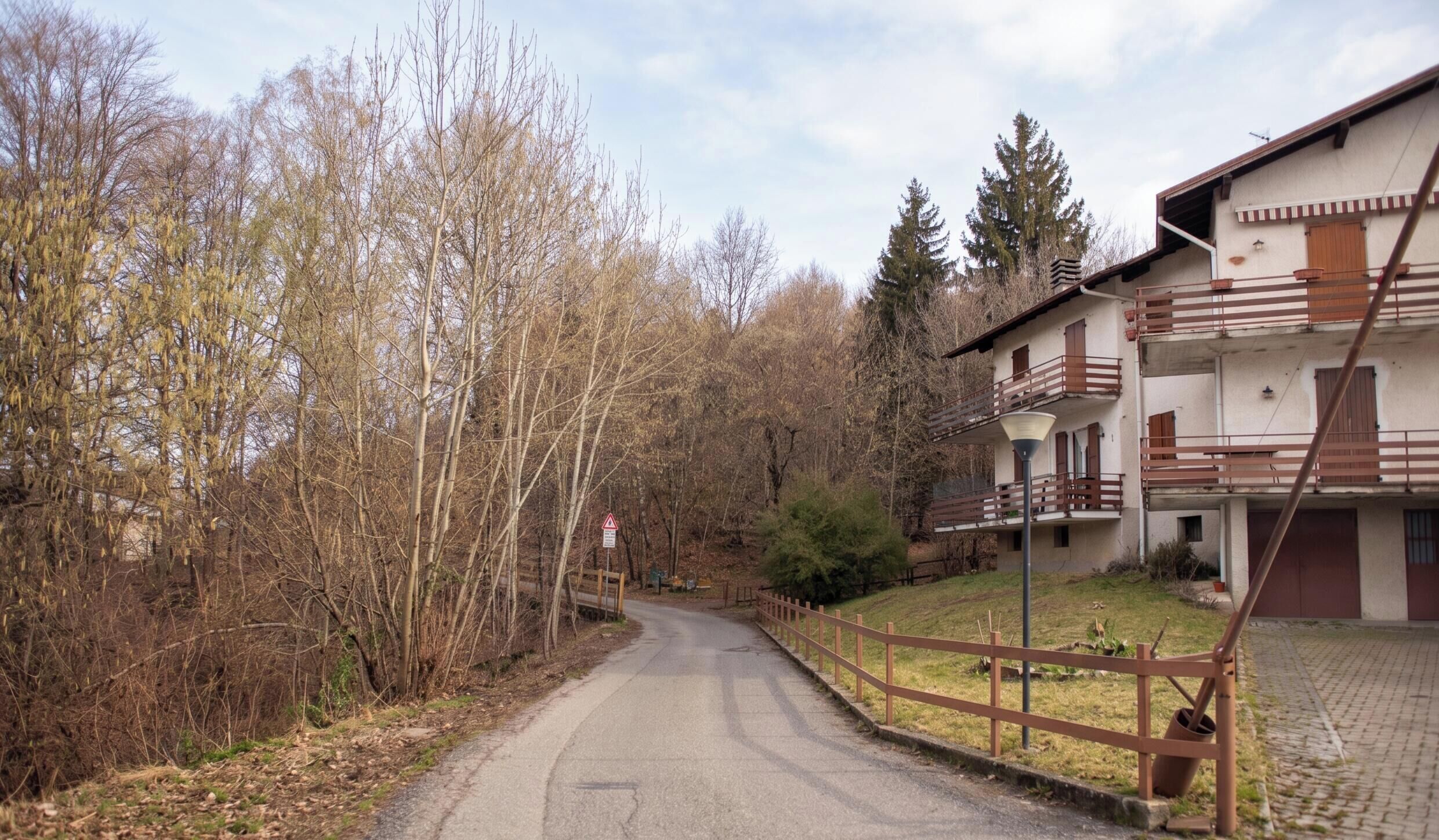 A two-story building with balconies, a paved road, and a wooded area.