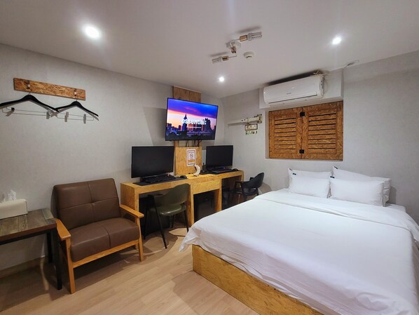 A hotel room with a bed, desk, two monitors, a chair, a TV, and an air conditioning unit. - ORAGO stay hotel (Suwon)