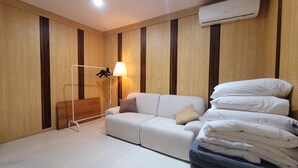A hotel room with a sofa, a lamp, a bed with pillows, and a wall-mounted air conditioner. - ORAGO stay hotel (Suwon)