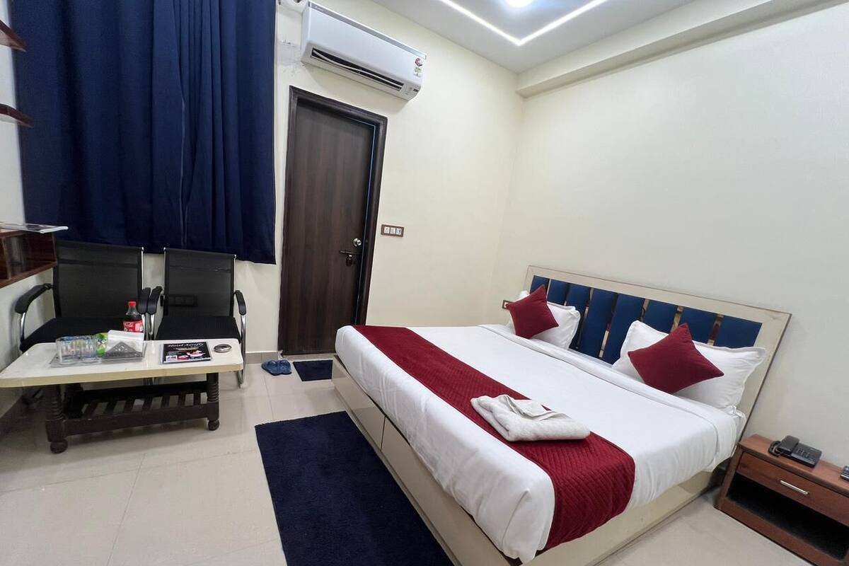 A hotel room with a bed, a desk, a chair, an air conditioner, and a door.