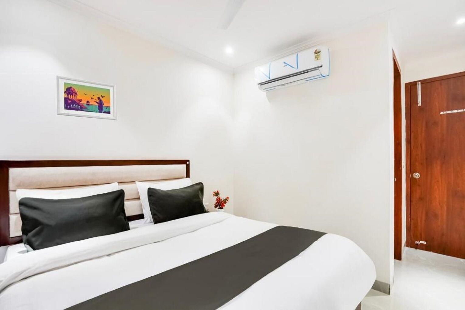 A hotel room with a bed, a picture on the wall, and an air conditioning unit.