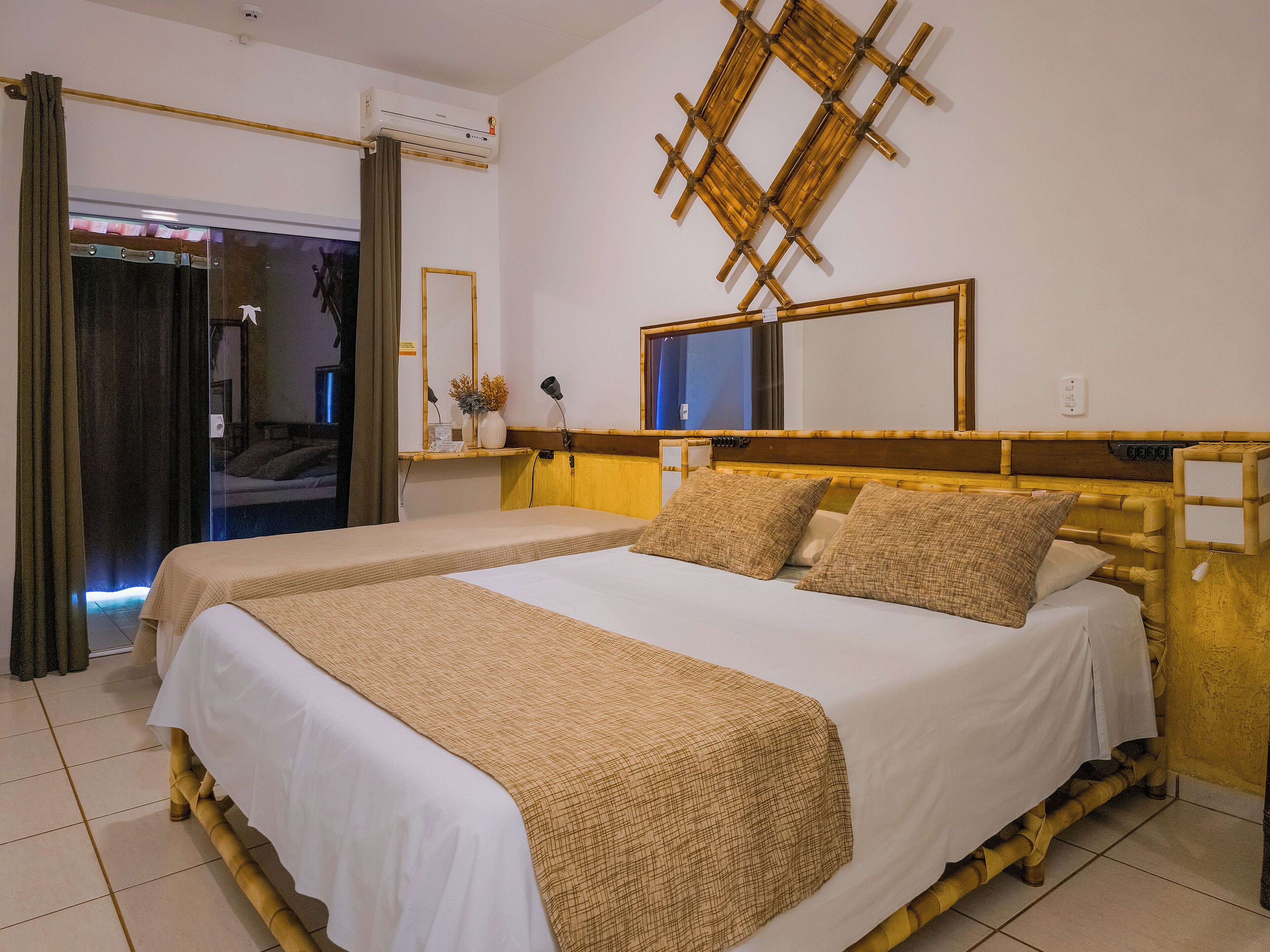 Quarto de hotel com duas camas, um espelho grande, um aparelho de ar condicionado e uma janela com vista.